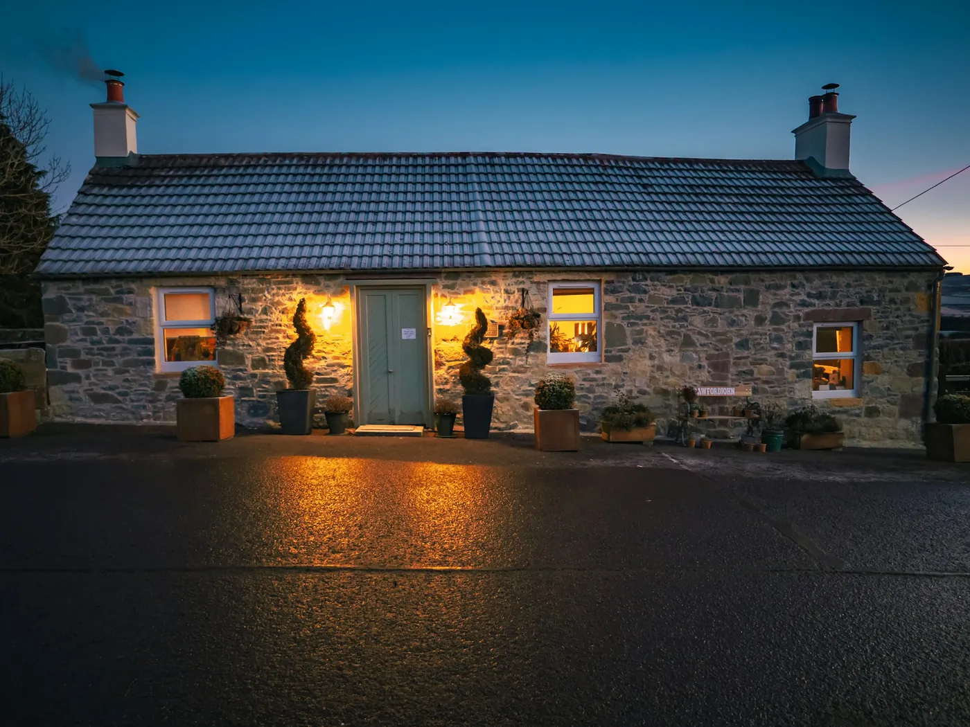 Stone cottage with its windows lit at dusk